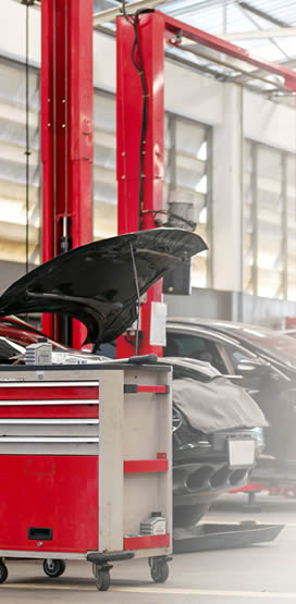 Taller mecànic en acció amb un vehicle amb el capó obert sent reparat i una caixa d'eines al lateral esquerre.